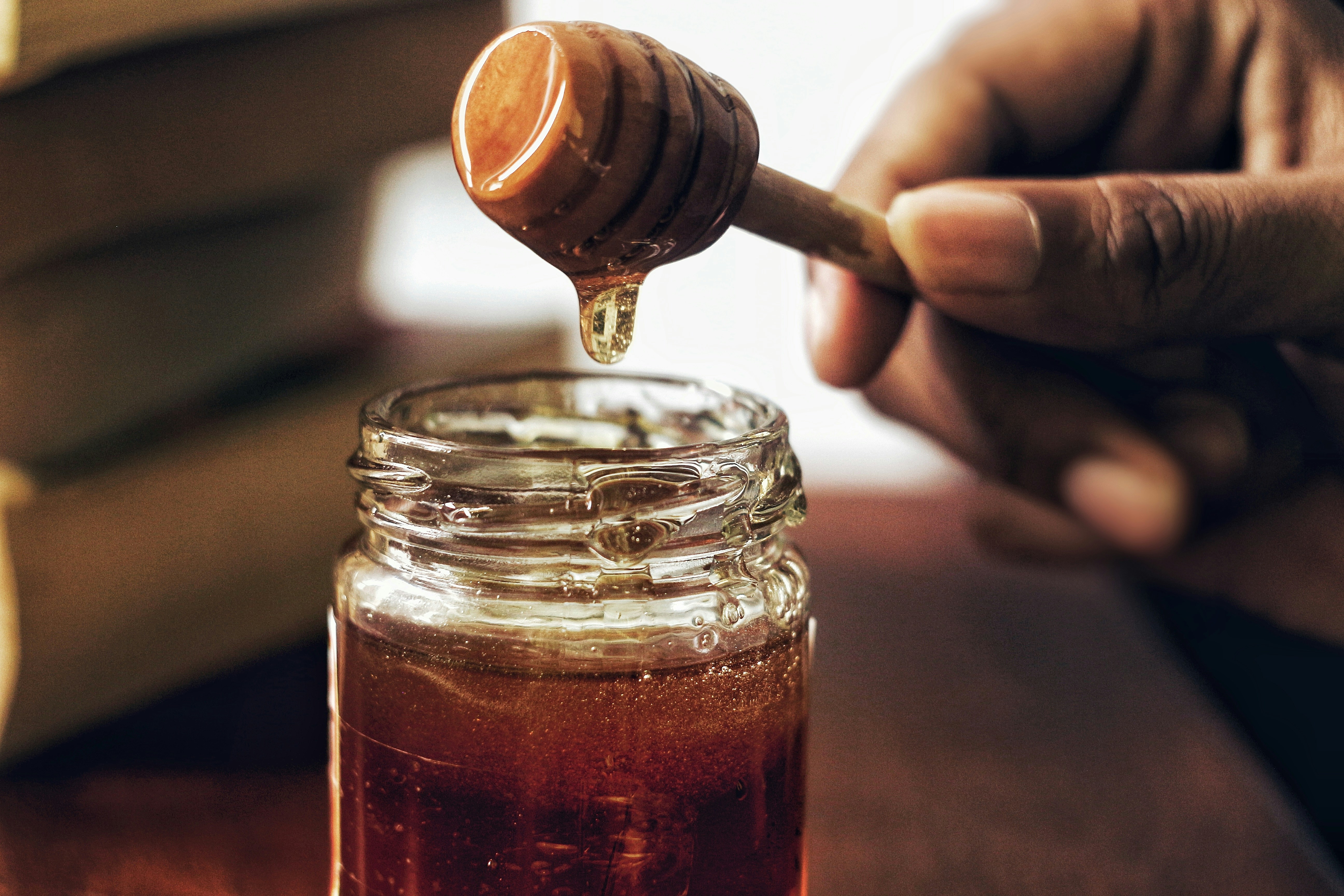 Honey dripping from dipper into jar on wooden table