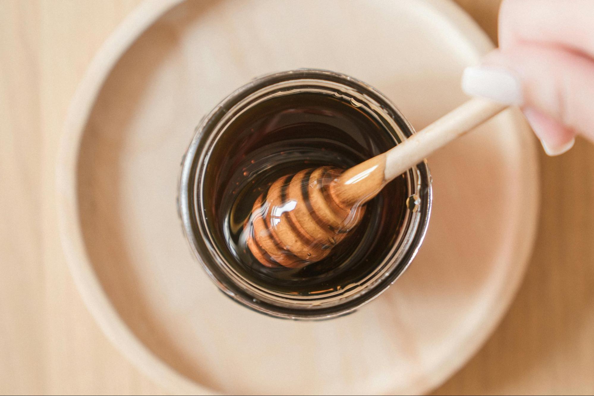 hand dipping honey dipper into jar