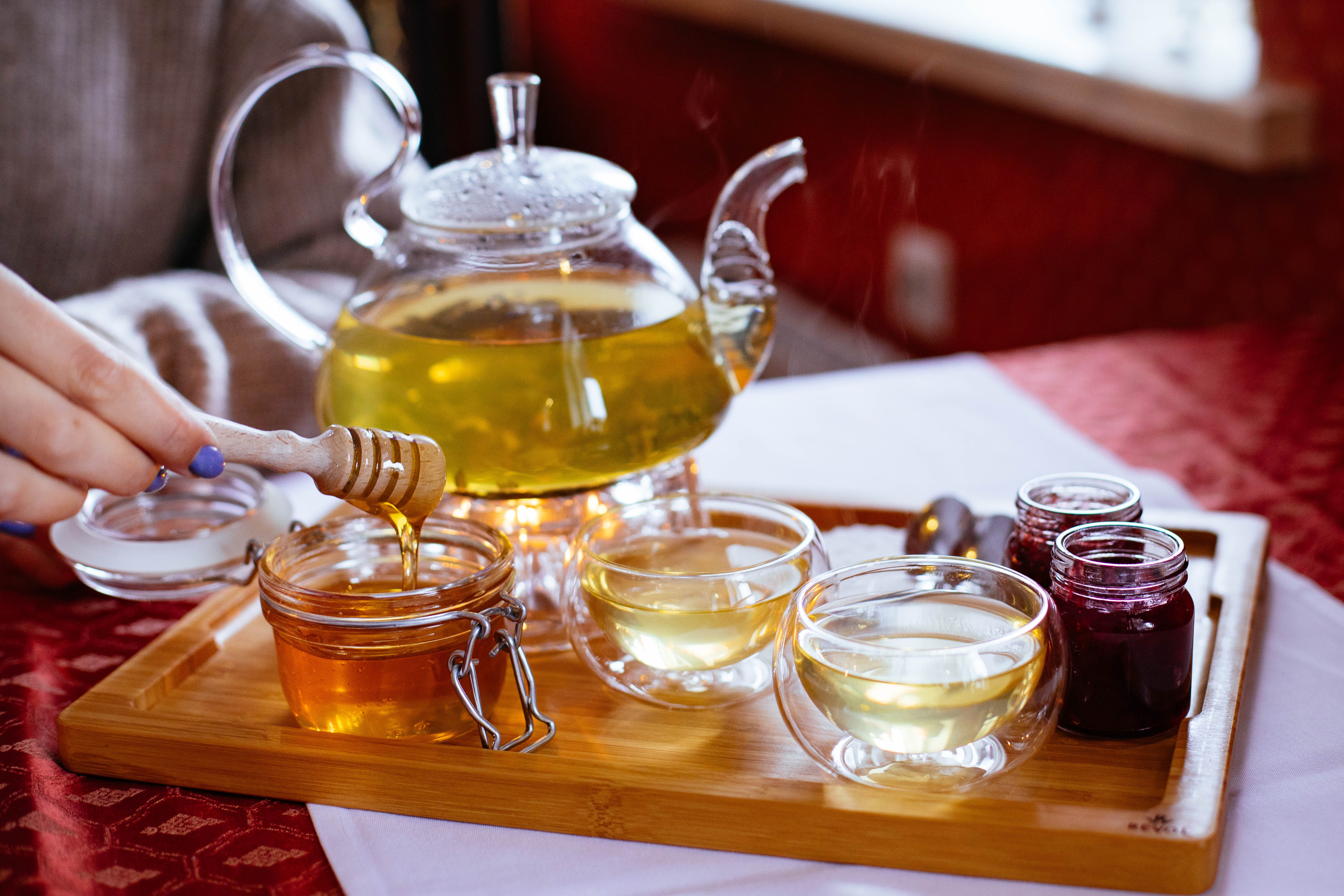 Person serving green tea and honey with jam on a wooden tray